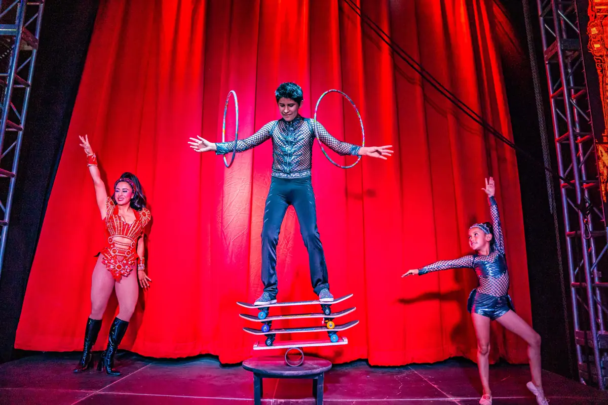 Skateboard balancing act with two hoops in front of a red curtain